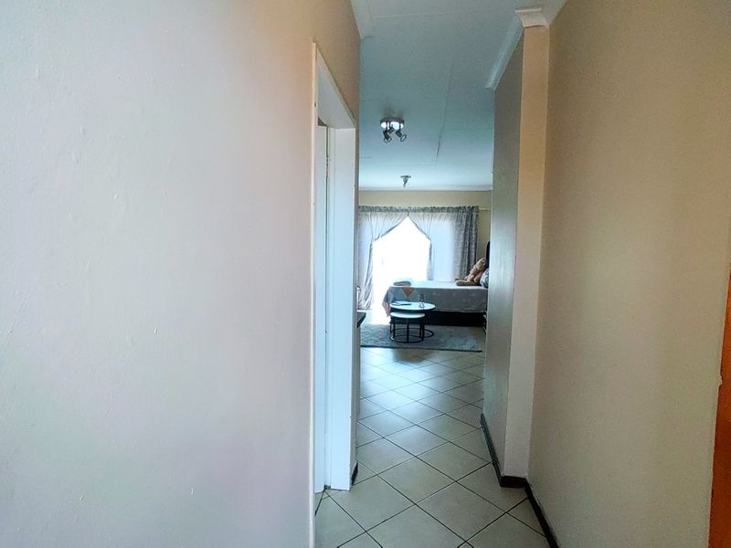 A view through a tiled hallway leading into a bedroom area, featuring neutral wall tones and standard ceiling finishes.