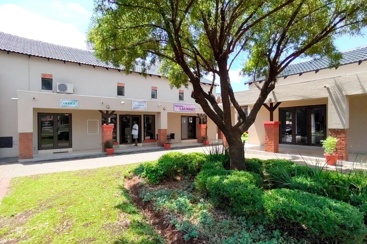 A well-maintained exterior courtyard area featuring paved walkways, landscaped garden beds, and multiple commercial-style glass entrance doors under a tiled roof.