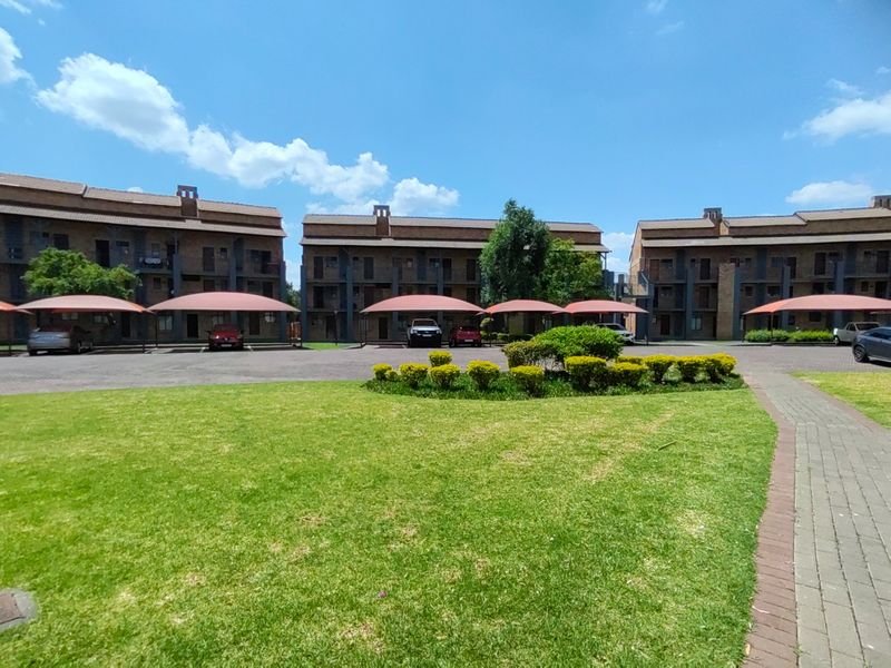Exterior view of a multi-story apartment complex featuring brick facades, covered parking bays, and well-maintained communal garden areas.