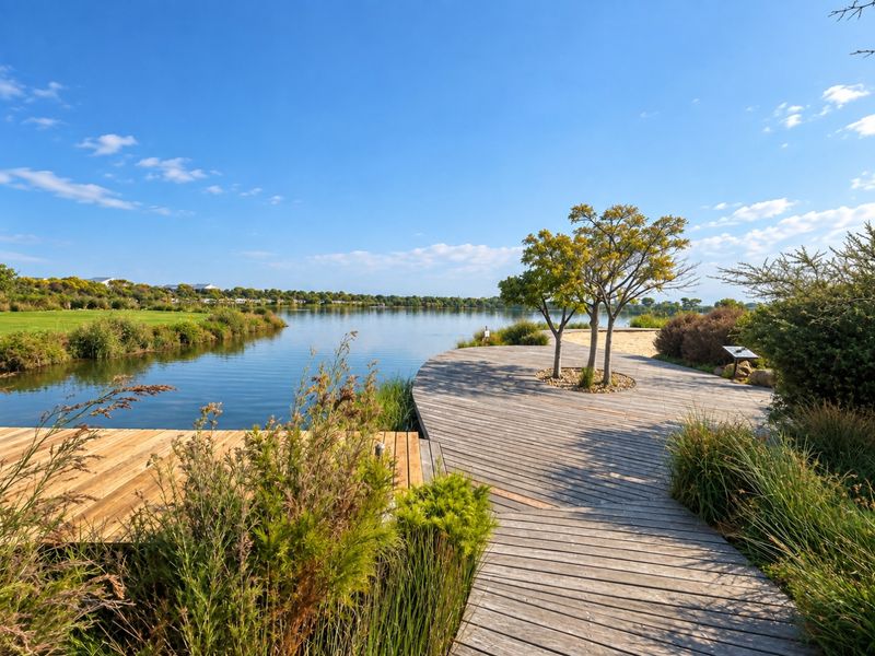 A scenic view of a tranquil lake featuring a well-maintained wooden boardwalk and landscaped garden area.