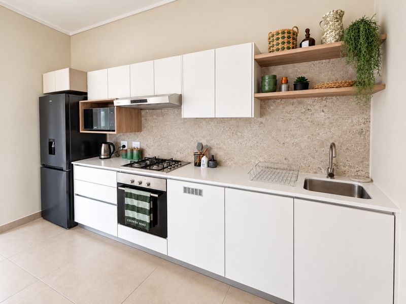 Modern kitchen featuring white cabinetry, stone countertops, a terrazzo-style backsplash, integrated gas hob, oven, and open shelving for a clean, contemporary aesthetic.