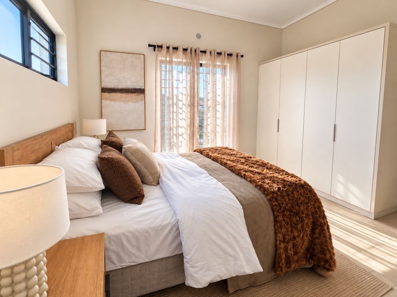 A well-lit bedroom featuring a spacious built-in wardrobe, neutral wall finishes, and a sliding door providing access to natural light.