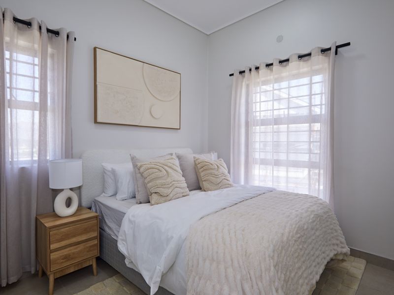 A bright and well-maintained bedroom featuring neutral tones, tiled flooring, and dual windows with fitted curtain rods.