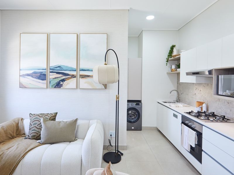 Modern open-plan apartment featuring a sleek kitchen with built-in appliances, stone-look backsplash, and a dedicated laundry cupboard, seamlessly integrated with the living area.