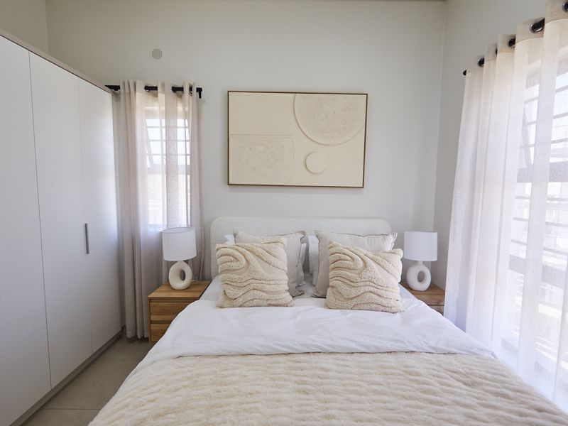 A well-maintained bedroom featuring neutral tones, built-in wardrobes, and ample natural light through large windows with installed curtain rails.