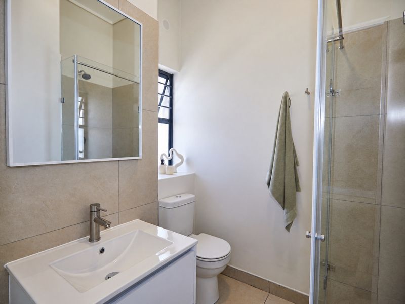 A modern bathroom featuring a vanity with basin, a toilet, and a glass-enclosed shower with neutral wall and floor tiling.