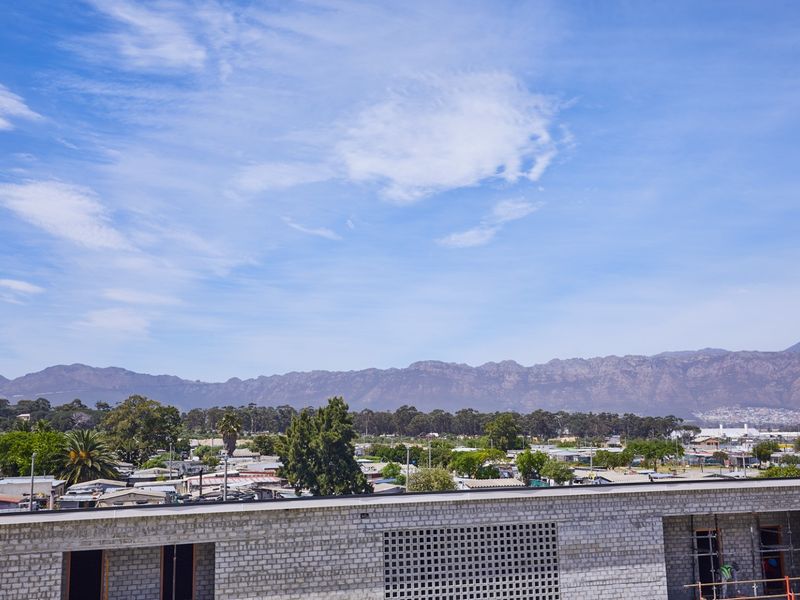 An elevated view overlooking a residential area with a scenic mountain range backdrop, featuring an unfinished brick building structure in the foreground.