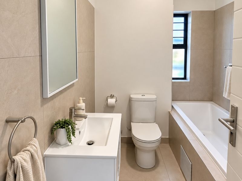 A modern, well-maintained bathroom featuring a wall-mounted vanity, a clean white basin, a toilet, and a tiled bathtub area with neutral finishes.