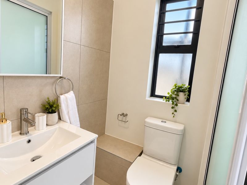 Modern bathroom featuring a sleek vanity cabinet, basin with mixer tap, wall-mounted mirror, and a clean tiled finish with a frosted glass window.