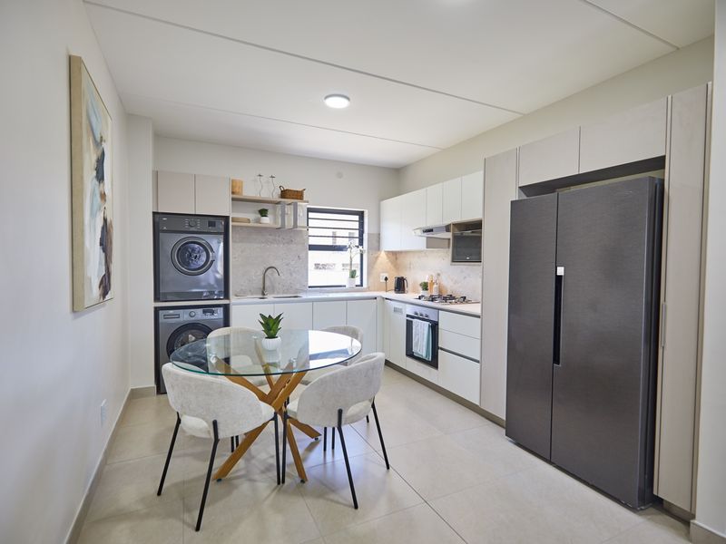 Modern open-plan kitchen featuring sleek cabinetry, integrated appliances, stacked laundry unit, and tiled flooring, seamlessly flowing into a dining area.