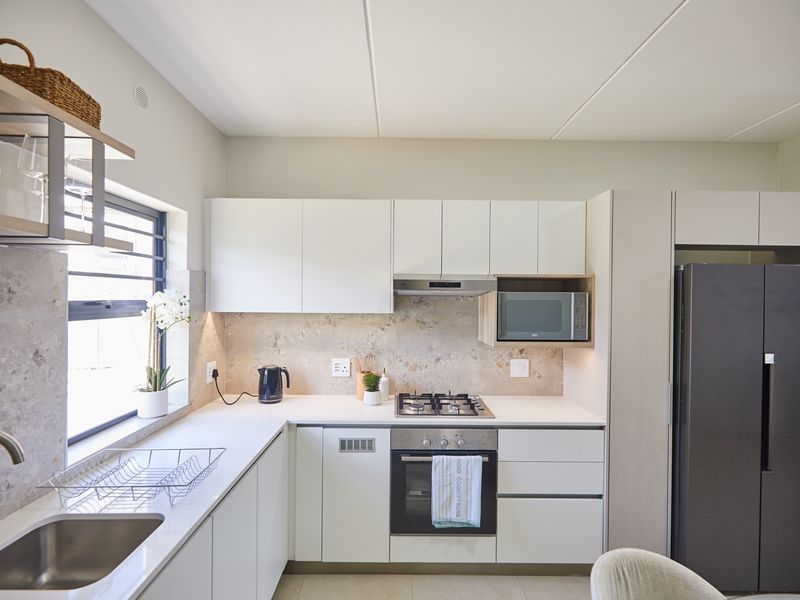 Modern kitchen featuring sleek white cabinetry, stone countertops, a gas hob, built-in oven, and integrated microwave with a stylish stone-look backsplash.