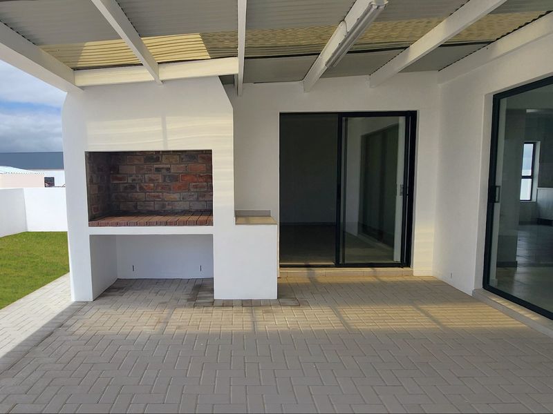 A covered patio area featuring a built-in brick braai, paved flooring, and sliding glass doors providing access to the interior living space.