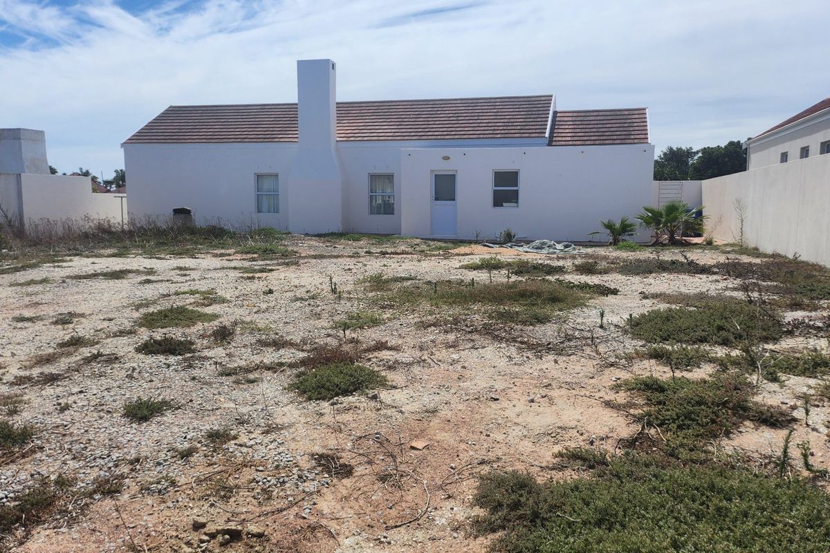 Rear view of the house featuring a tiled roof, prominent chimney, and a large, undeveloped garden area enclosed by boundary walls.