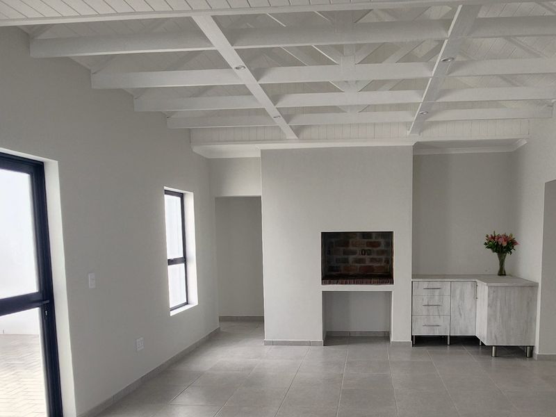 Bright and spacious living area featuring a high exposed beam ceiling, tiled floors, and a built-in fireplace with adjacent cabinetry.