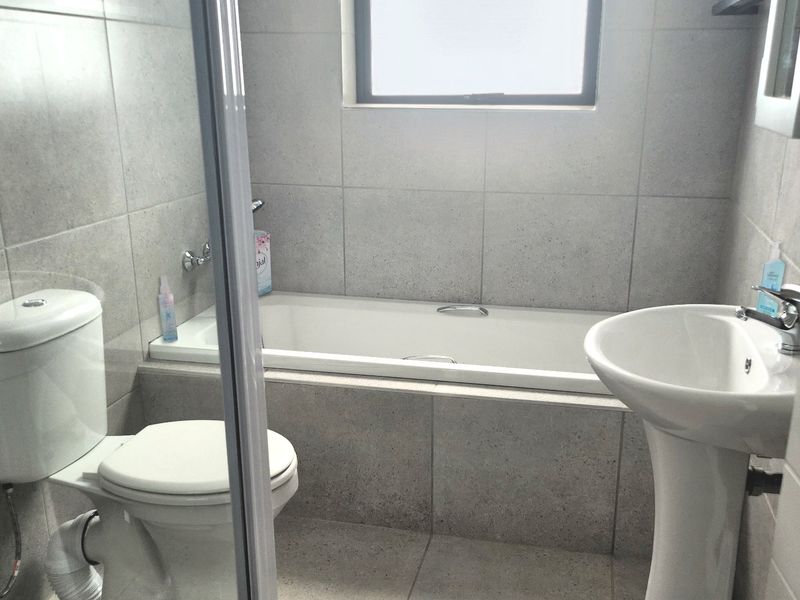 A modern bathroom featuring a built-in bathtub, pedestal basin, toilet, and tiled finishes throughout, offering a clean and functional space.