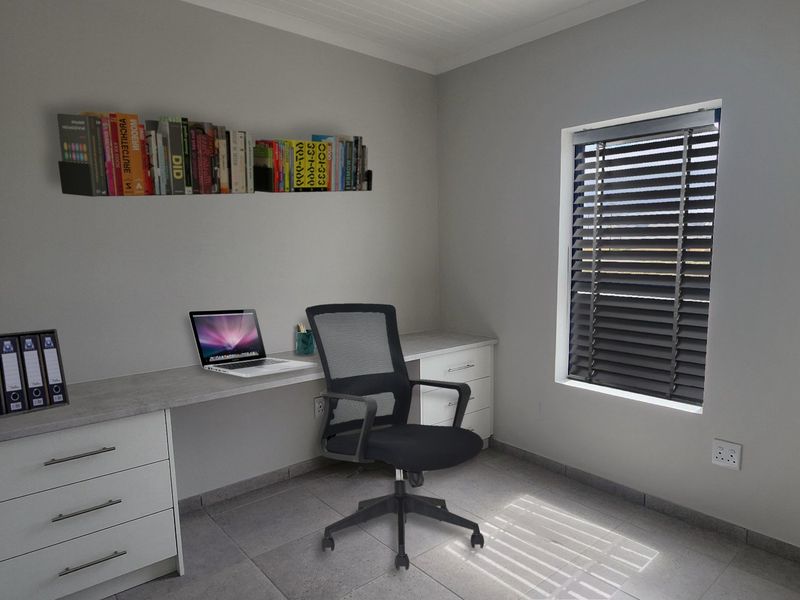 A functional home office featuring a built-in desk with integrated storage drawers, tiled flooring, and venetian blinds for adjustable natural light.