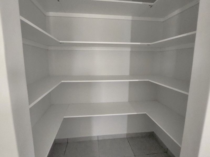 A clean, empty walk-in pantry or scullery featuring white built-in shelving and tiled flooring, providing ample storage space.