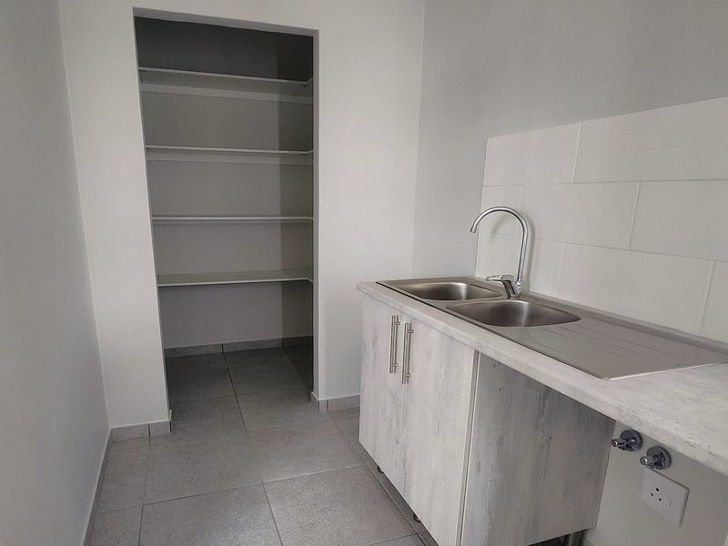 A clean and functional scullery featuring a double bowl sink, laminate countertop, tiled splashback, and a convenient walk-in pantry with built-in shelving.