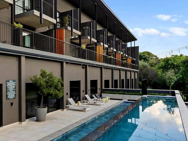Modern apartment complex featuring a sleek lap pool, paved patio area, and private balconies with contemporary dark exterior finishes.