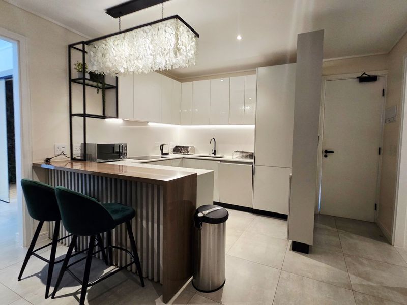 Modern kitchen featuring sleek white cabinetry, stone countertops, a breakfast bar, and integrated lighting, finished with contemporary tiled flooring.