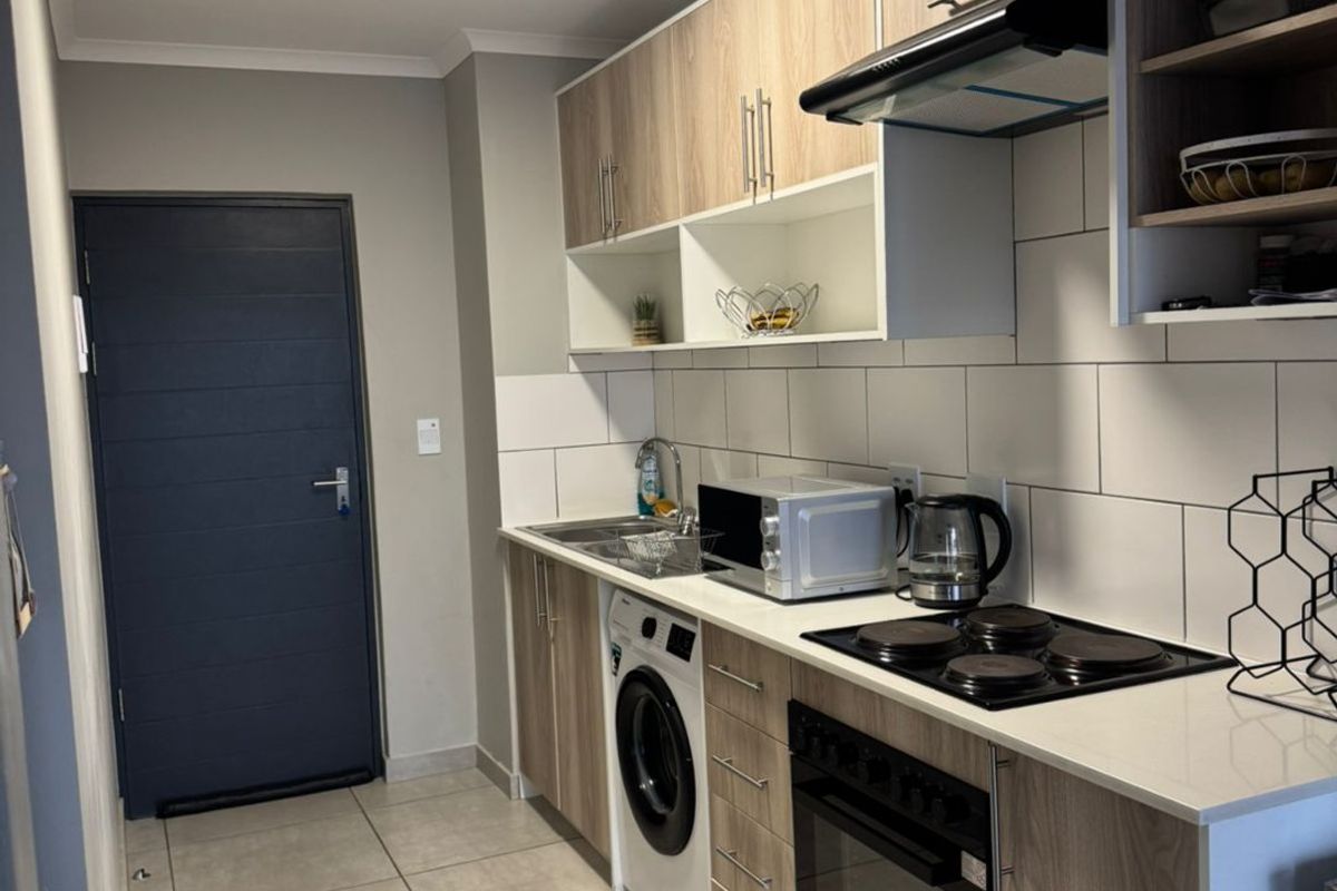 Modern kitchen featuring light wood-tone cabinetry, integrated appliances, electric hob, oven, extractor fan, and tiled backsplash with neutral floor tiles.