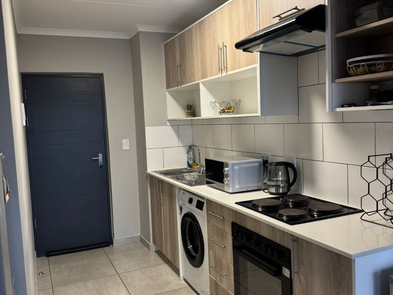 Modern kitchen featuring light wood-tone cabinetry, integrated appliances, electric hob, oven, extractor fan, and tiled backsplash with neutral floor tiles.