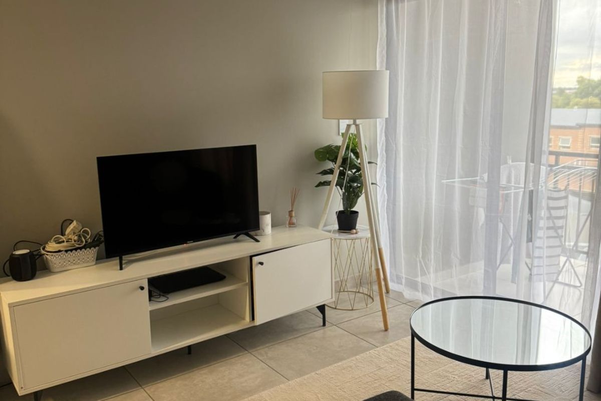 A well-maintained living room featuring neutral wall tones, tiled flooring, and a large sliding glass door providing access to an outdoor balcony area.