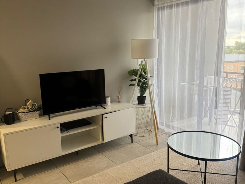 A well-maintained living room featuring neutral wall tones, tiled flooring, and a large sliding glass door providing access to an outdoor balcony area.