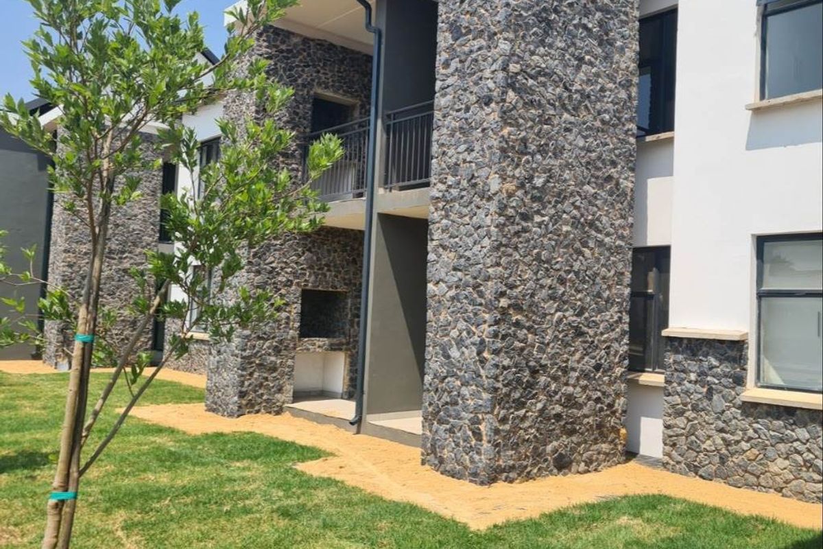 Rear view of a modern apartment building featuring stone cladding, a built-in braai area, and a private balcony.