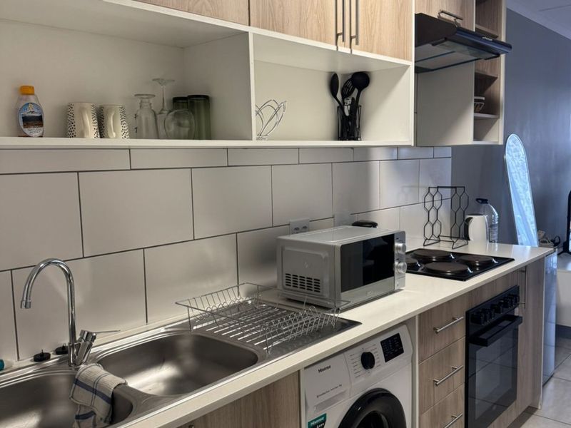 Modern kitchen featuring light wood-finish cabinetry, tiled backsplash, integrated oven and hob, and a built-in washing machine.