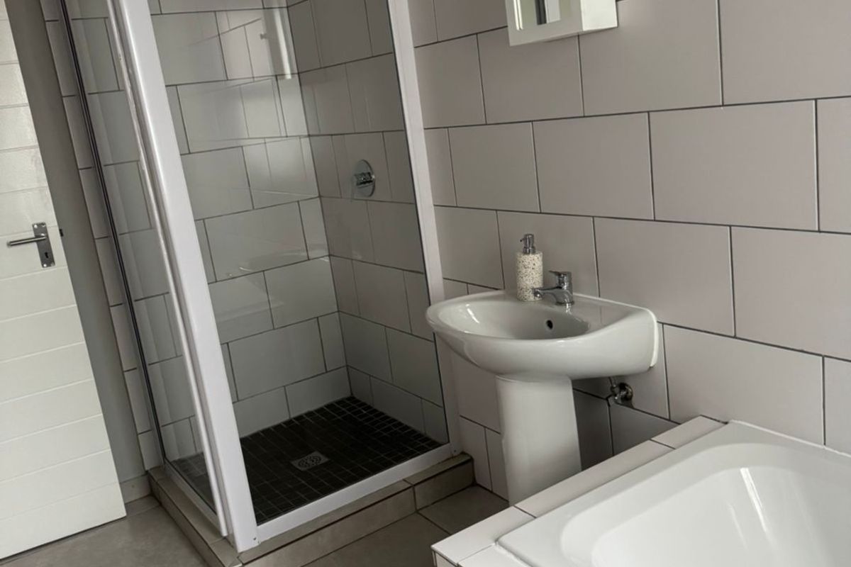 A clean, functional bathroom featuring a separate shower enclosure, pedestal basin, and bathtub with neutral wall and floor tiling.