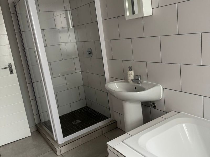 A clean, functional bathroom featuring a separate shower enclosure, pedestal basin, and bathtub with neutral wall and floor tiling.