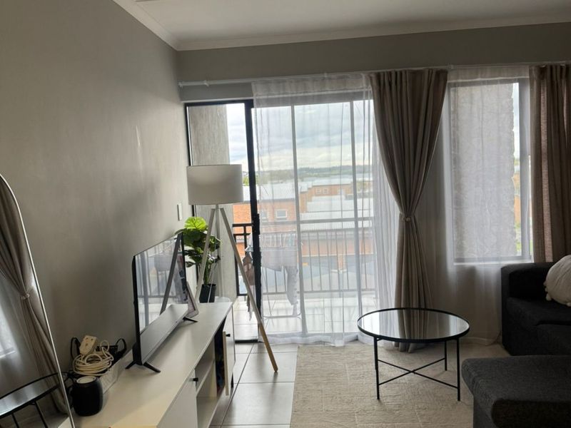 A bright living room featuring tiled flooring and a large sliding glass door that provides access to a balcony with an outdoor view.