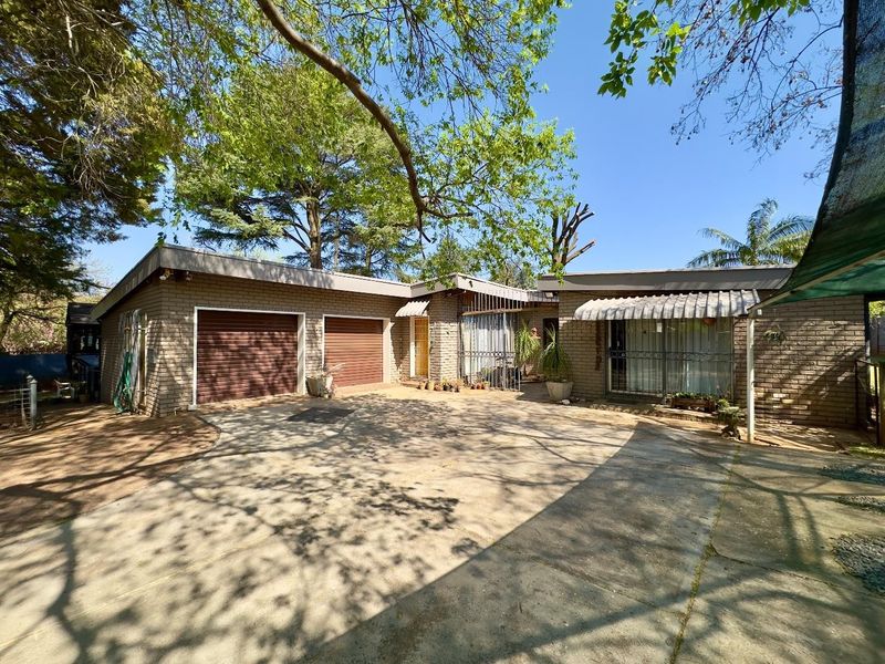 Front exterior view of a single-story brick house featuring a double garage, concrete driveway, and established trees.