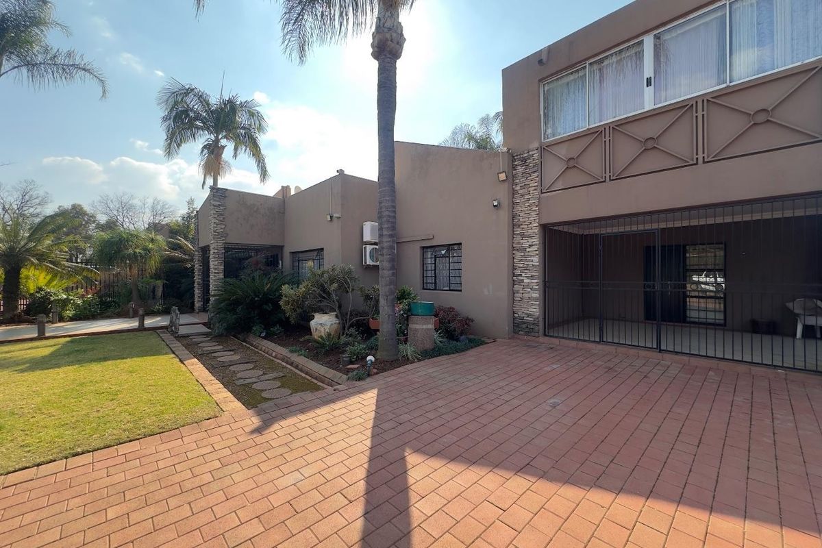 Rear exterior view featuring a paved driveway, stone-clad accents, security gates, and a well-maintained lawn area.