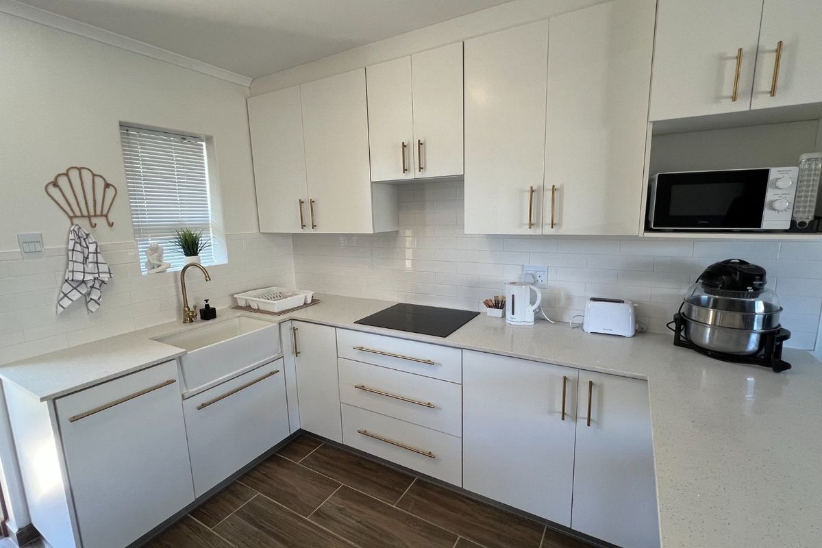 Modern kitchen featuring white cabinetry, quartz countertops, a farmhouse sink, brass hardware, and a subway tile backsplash with an integrated induction hob.