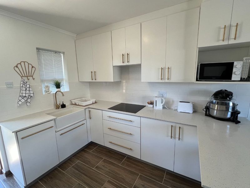 Modern kitchen featuring white cabinetry, quartz countertops, a farmhouse sink, brass hardware, and a subway tile backsplash with an integrated induction hob.