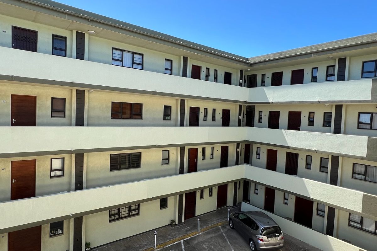 Exterior view of a multi-story apartment complex featuring open-air walkways, secure unit entrances, and a paved courtyard with designated parking bays.