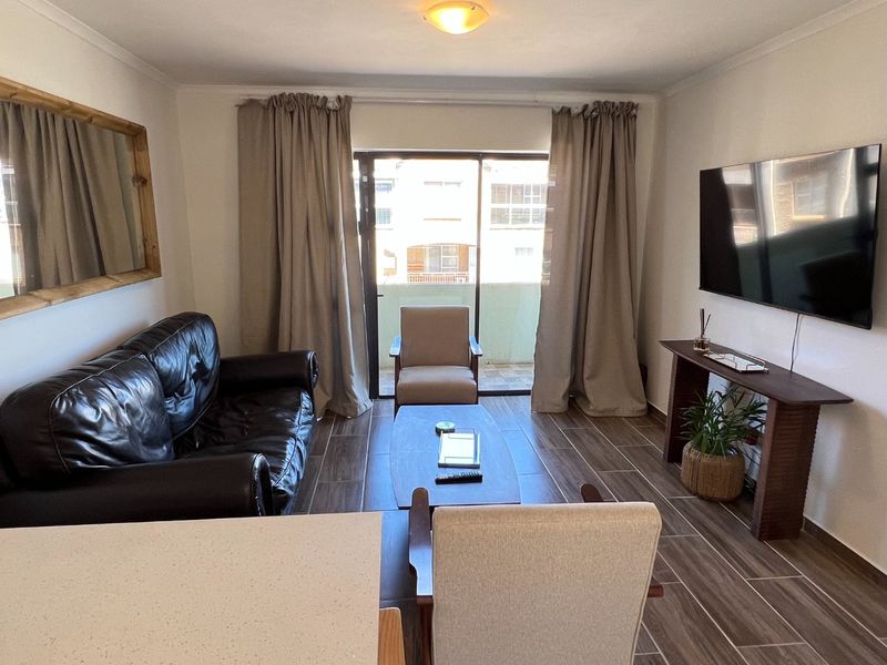 A well-maintained living room featuring modern tiled flooring and a sliding glass door that provides access to an outdoor balcony area.
