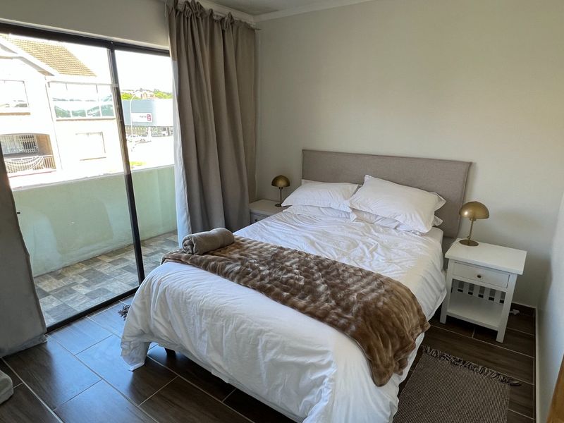 A well-maintained bedroom featuring modern tiled flooring and a large sliding glass door providing access to an outdoor balcony area.