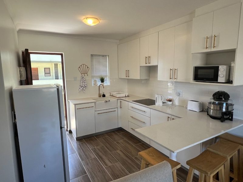Modern kitchen featuring white cabinetry, quartz countertops, an apron front sink, brass fixtures, and a breakfast bar, complemented by wood-look tile flooring.