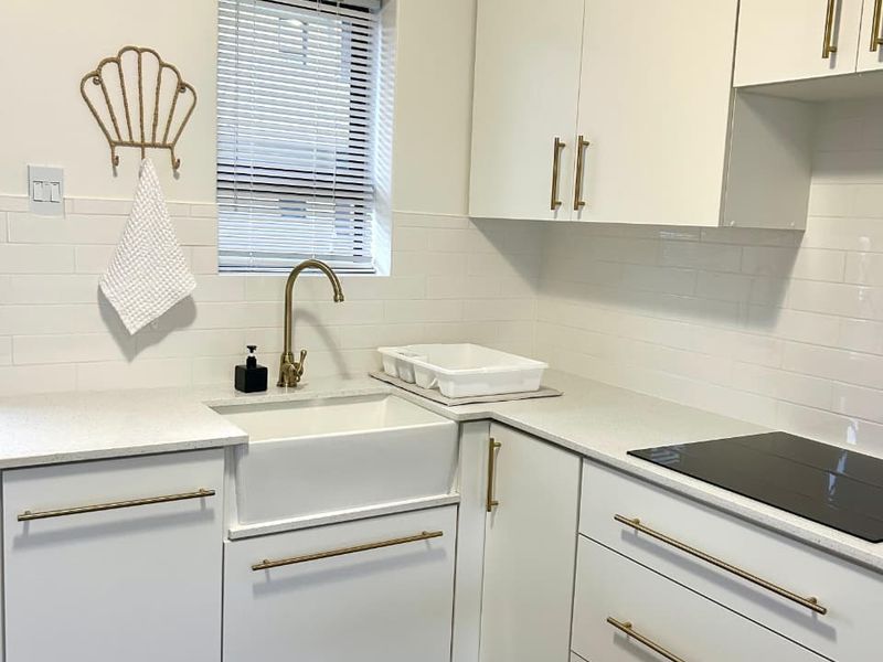 Modern kitchen featuring white shaker cabinetry, brass hardware, quartz countertops, a farmhouse sink, and a built-in induction hob with subway tile backsplash.
