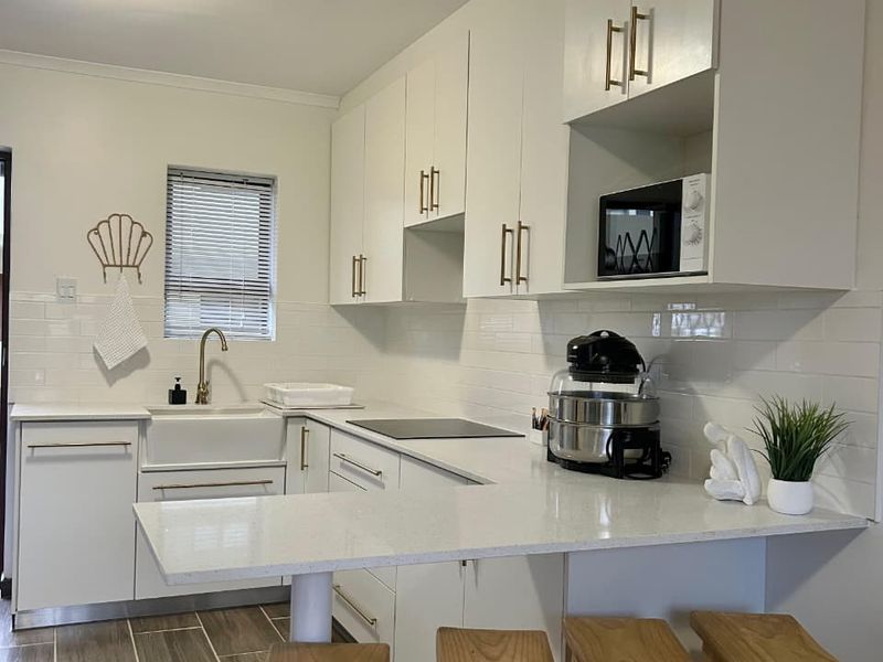 Modern kitchen featuring white cabinetry, quartz countertops, an apron-front sink with brass fixtures, and a subway tile backsplash with wood-look tile flooring.