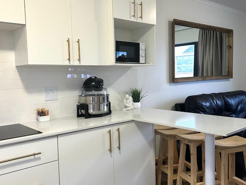 Modern open-plan kitchen featuring white cabinetry, stone countertops, subway tile backsplash, and a convenient breakfast bar with integrated hob and microwave.