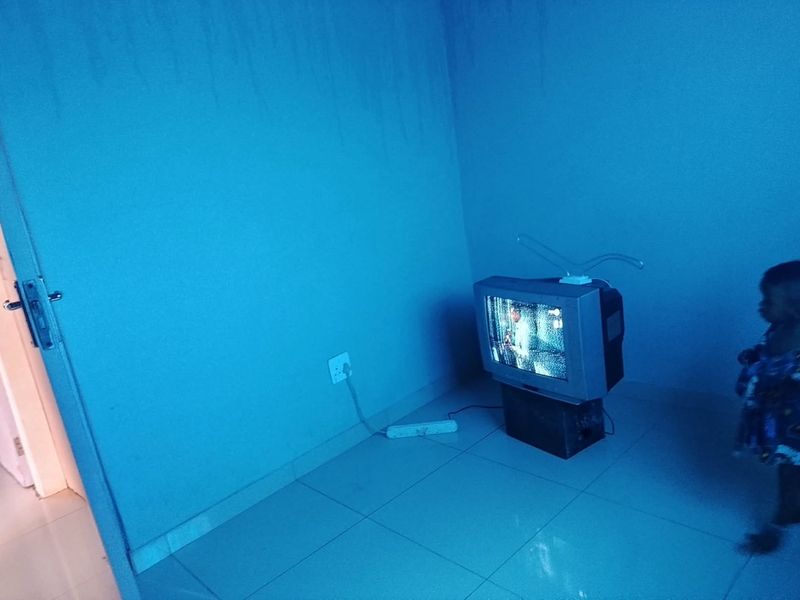 A sparsely furnished living area featuring tiled flooring and visible water damage on the wall, requiring maintenance and cosmetic updates.