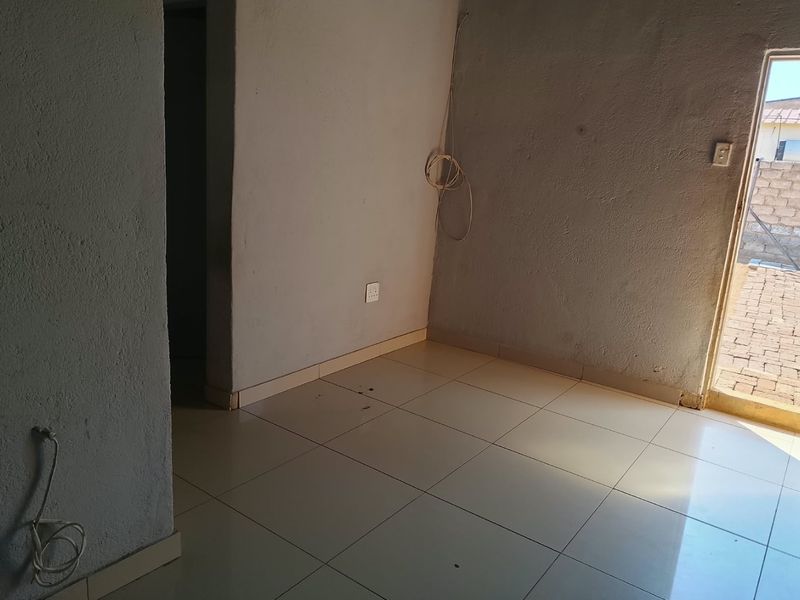 An empty living area featuring tiled flooring, exposed electrical wiring, and direct access to an outdoor space.