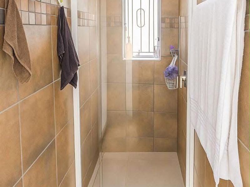 A compact bathroom featuring a walk-in shower with a glass enclosure, tiled walls, and a small window with security bars.