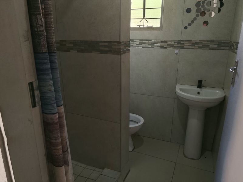 A functional bathroom featuring a pedestal basin, toilet, and shower area with tiled finishes and a small window for natural light.