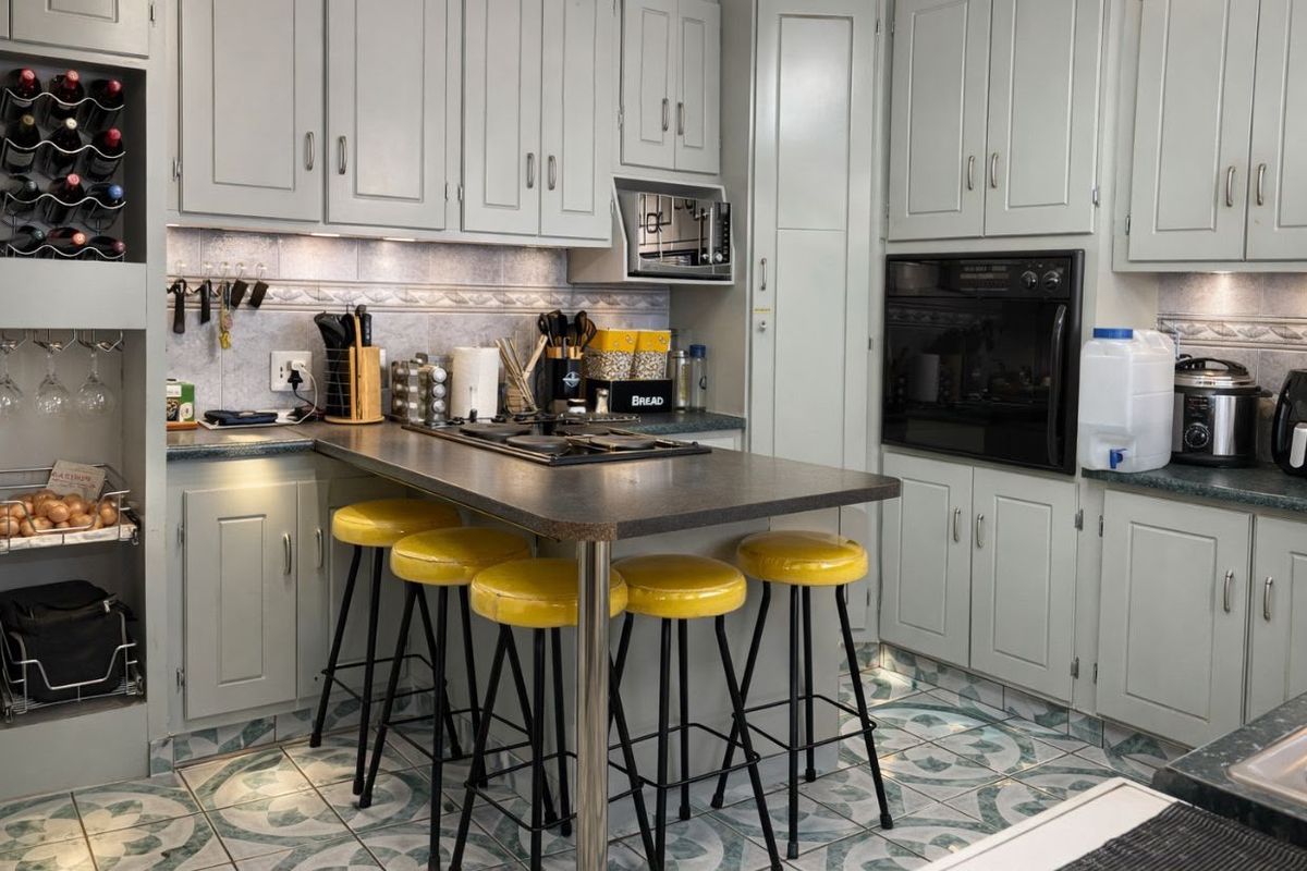 A functional kitchen featuring light grey cabinetry, dark laminate countertops, a built-in oven, gas hob, and decorative tiled flooring with integrated breakfast bar seating.