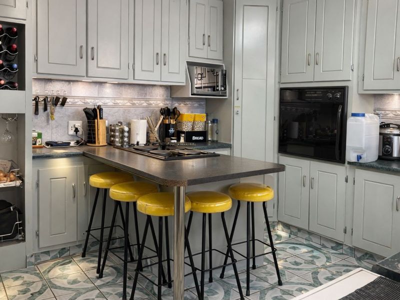 A functional kitchen featuring light grey cabinetry, dark laminate countertops, a built-in oven, gas hob, and decorative tiled flooring with integrated breakfast bar seating.